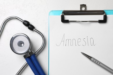 Photo of Clipboard with word Amnesia, pen and stethoscope on white table, flat lay