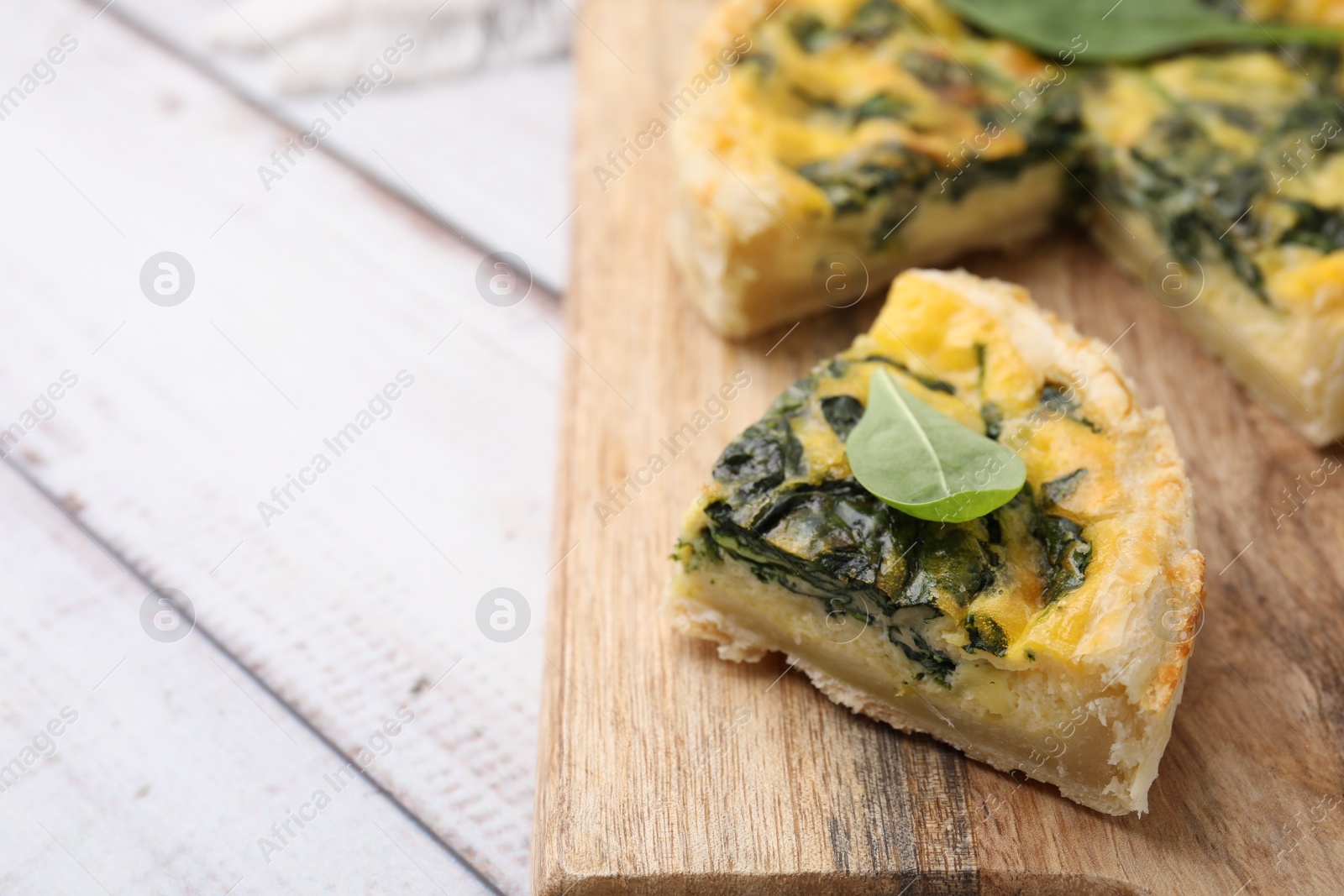 Photo of Piece of delicious pie with spinach on white wooden table, closeup. Space for text