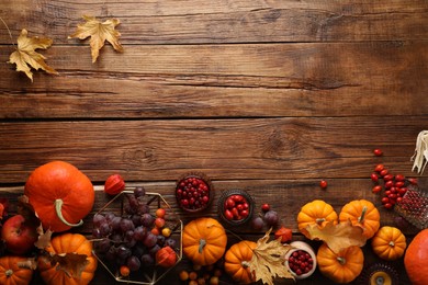 Photo of Flat lay composition with autumn leaves, berries and pumpkins on wooden table, space for text