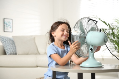 Little girl enjoying air flow from fan at home. Summer heat