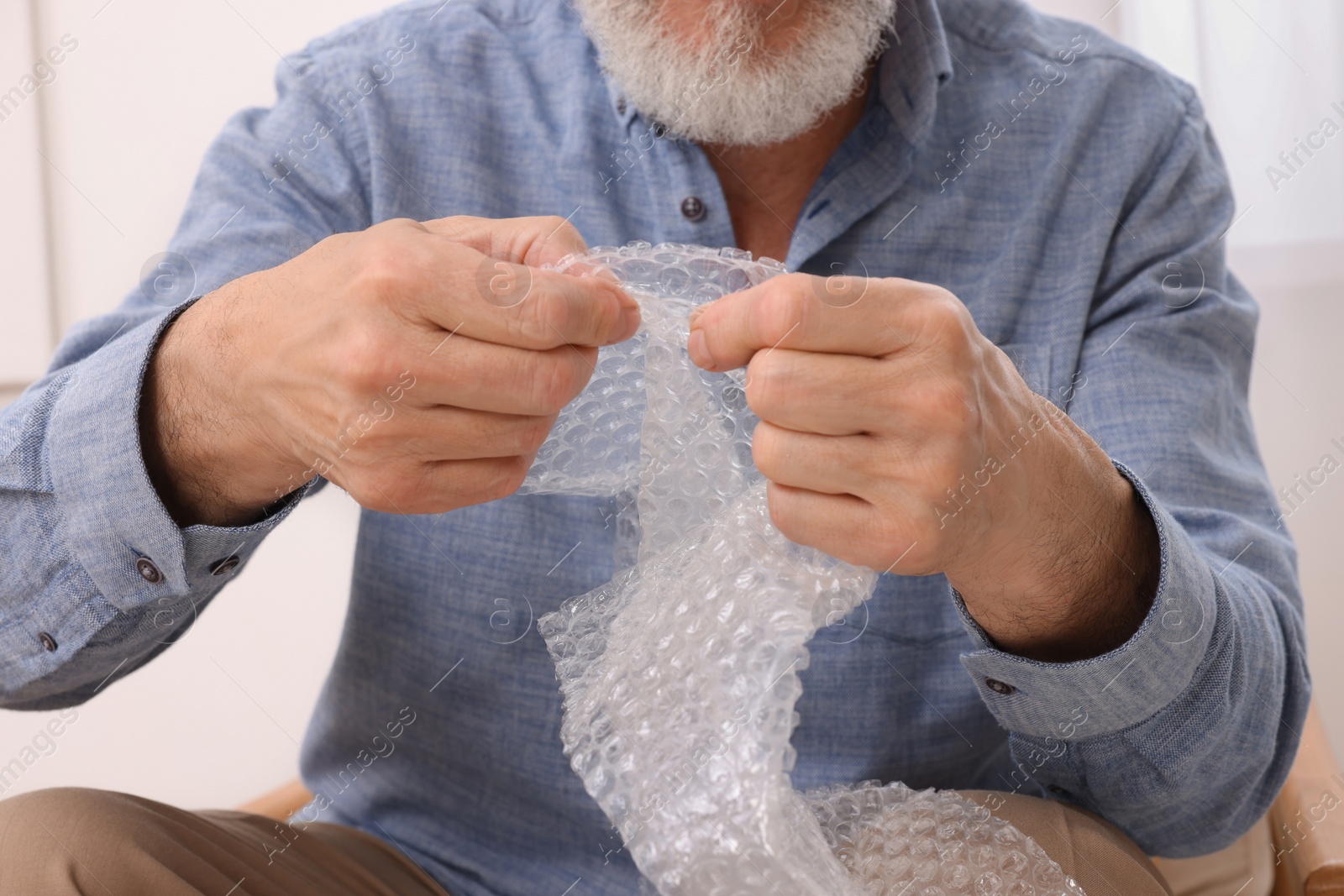 Photo of Senior man popping bubble wrap at home, closeup. Stress relief