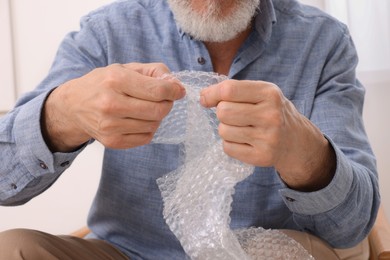 Senior man popping bubble wrap at home, closeup. Stress relief