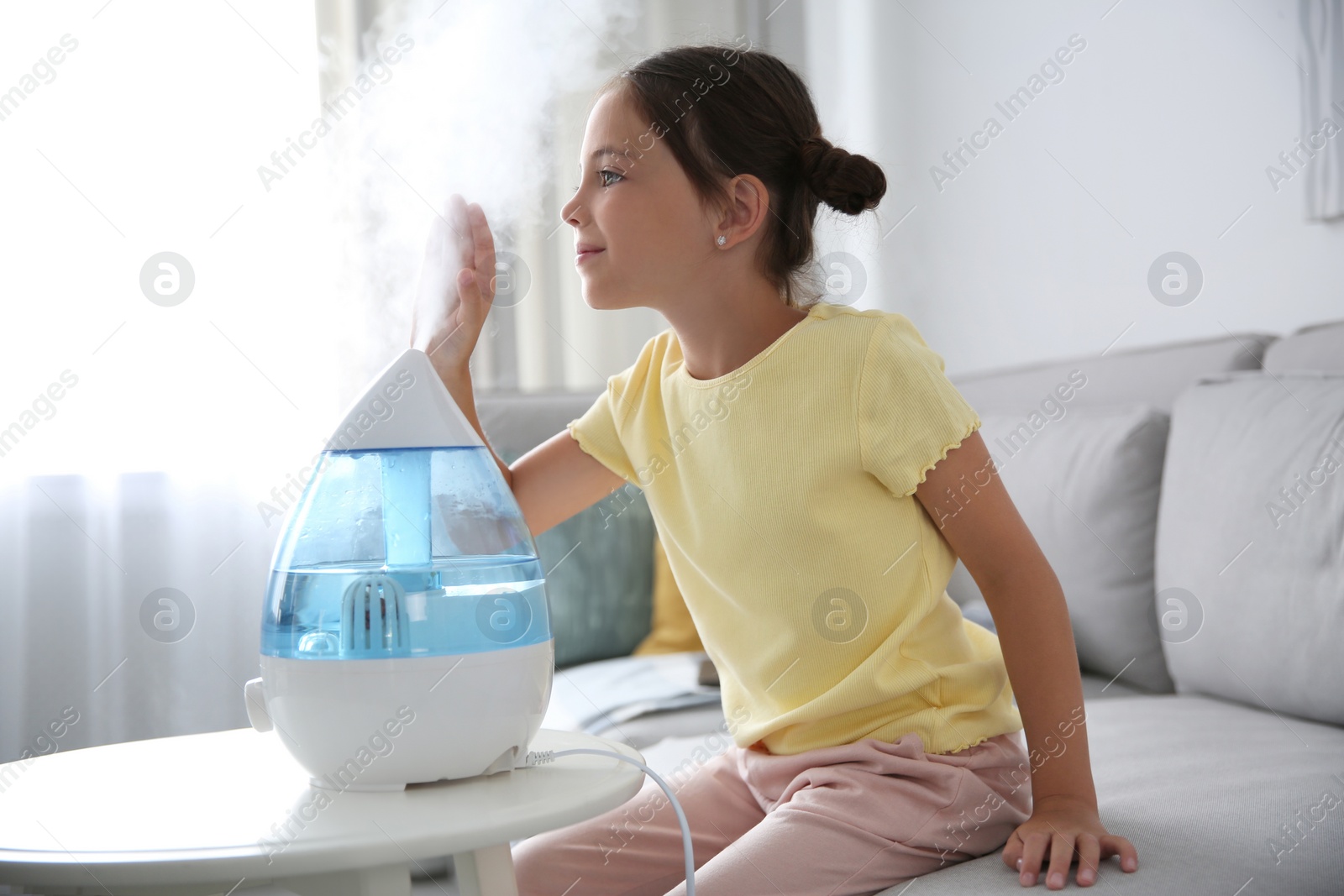 Photo of Little girl near modern air humidifier at home