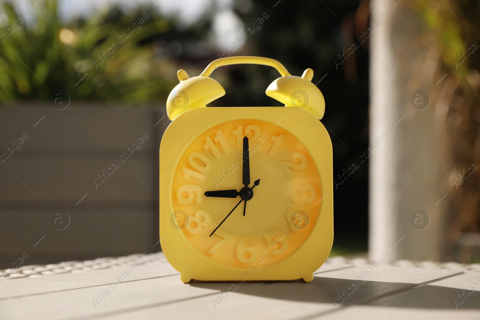 Photo of Yellow alarm clock on white wooden table outdoors at sunny morning