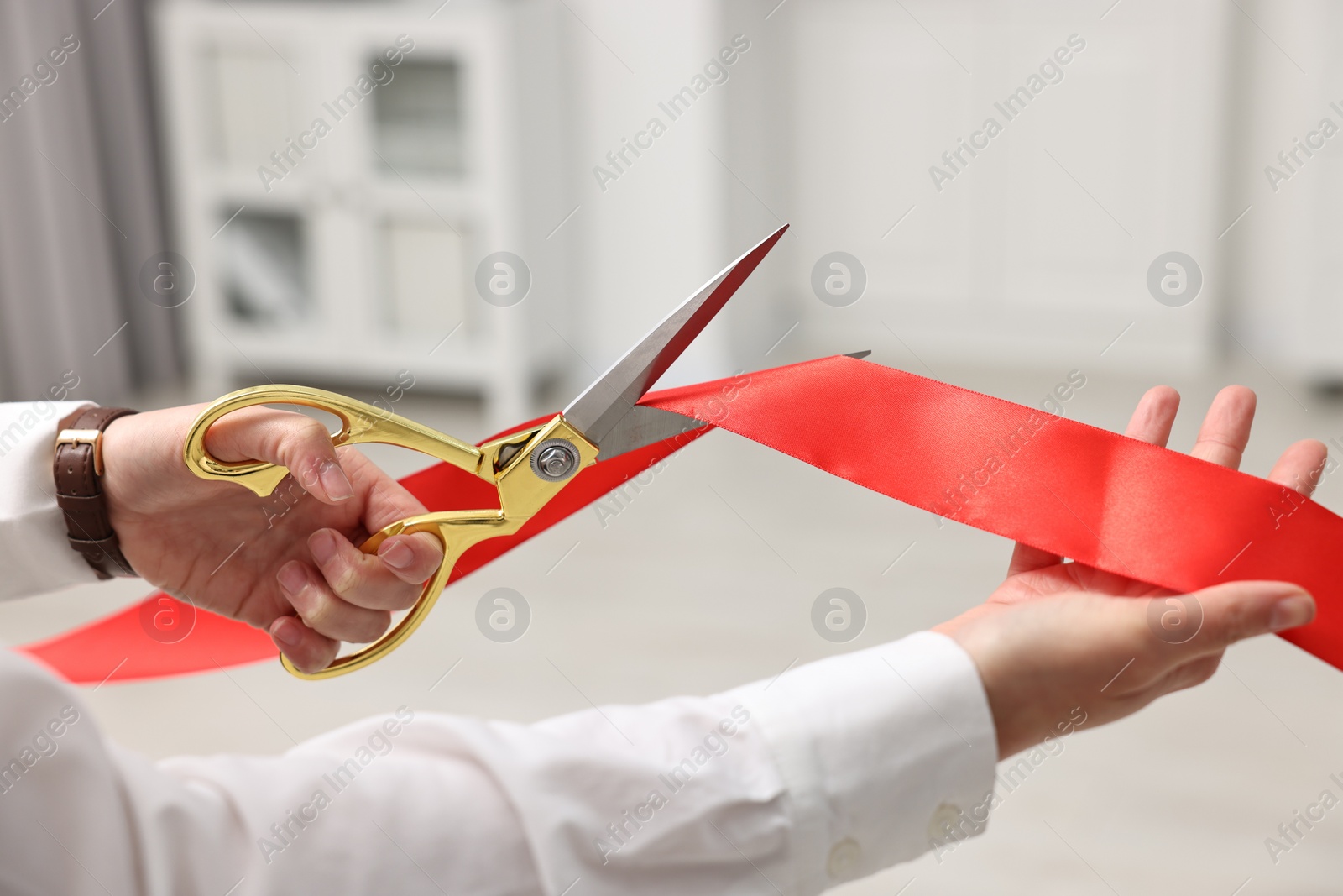 Photo of Woman cutting red ribbon with scissors indoors, closeup