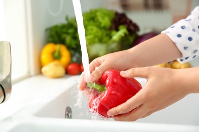 Woman washing fresh red bell pepper in kitchen sink, closeup