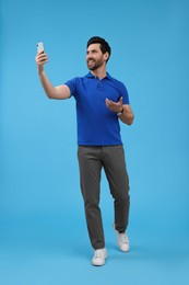 Photo of Smiling man taking selfie with smartphone on light blue background