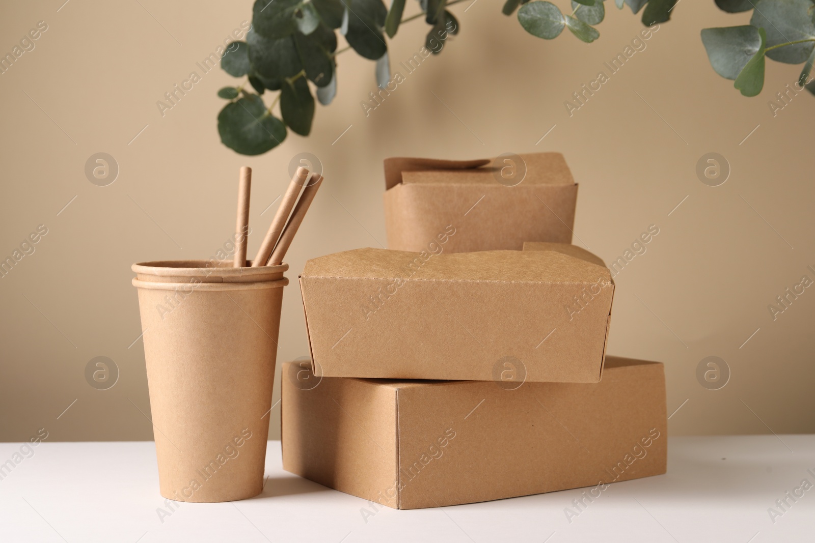 Photo of Eco friendly food packaging. Paper containers, straws and eucalyptus branches on white table against beige background