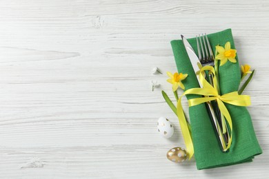Photo of Cutlery set, Easter eggs and narcissuses on white wooden table, flat lay. Space for text