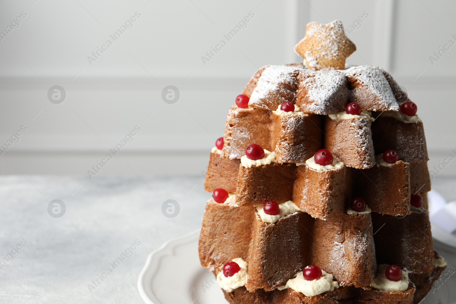 Photo of Delicious Pandoro Christmas tree cake with powdered sugar and berries on white table, closeup. Space for text