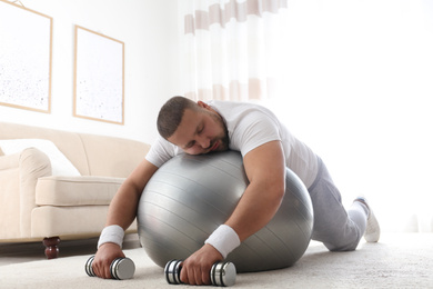 Lazy overweight man with sport equipment sleeping on floor at home