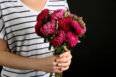 Woman with bouquet of beautiful asters on black background, closeup. Autumn flowers