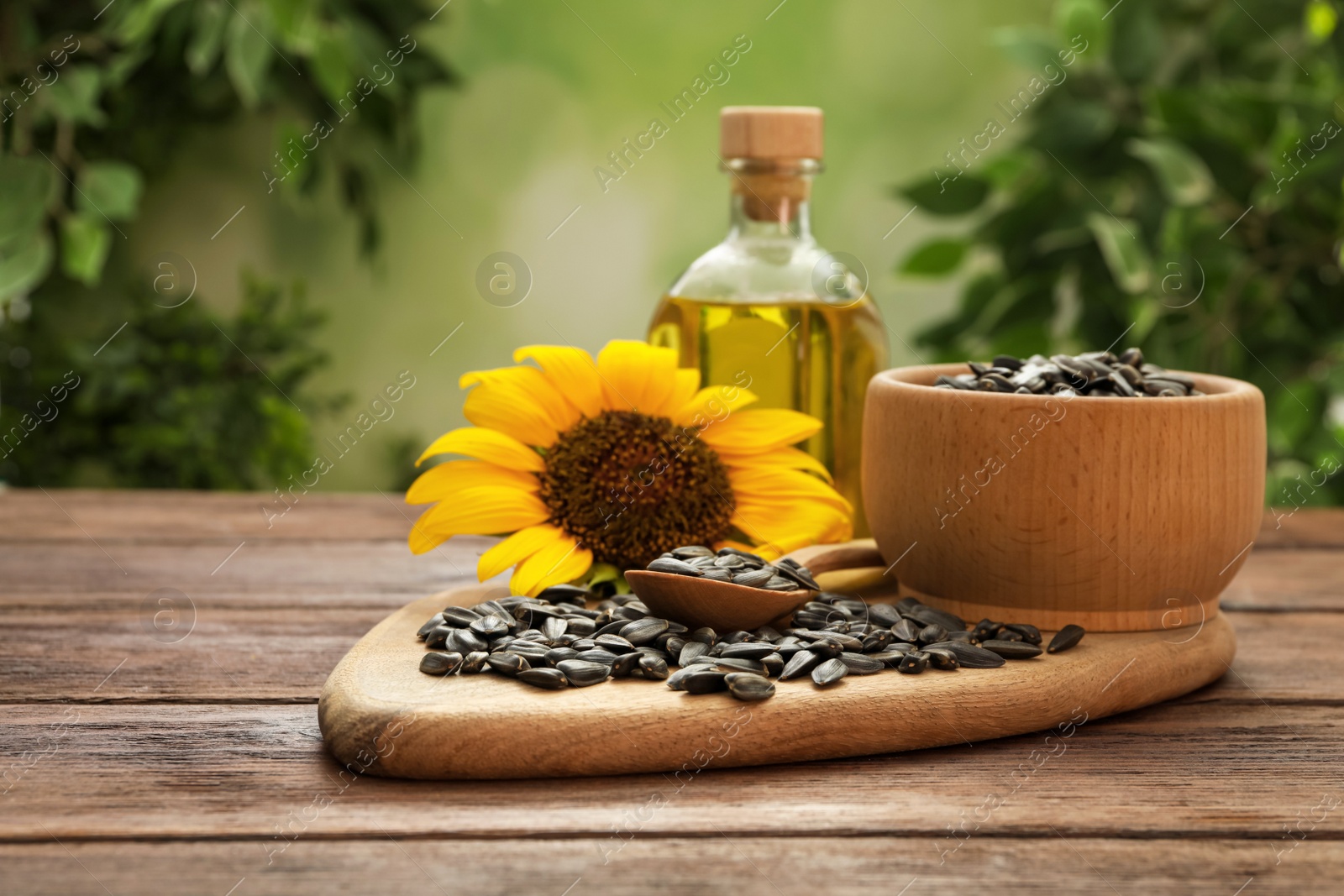 Photo of Sunflower, seeds and bottle of oil on wooden table against blurred background