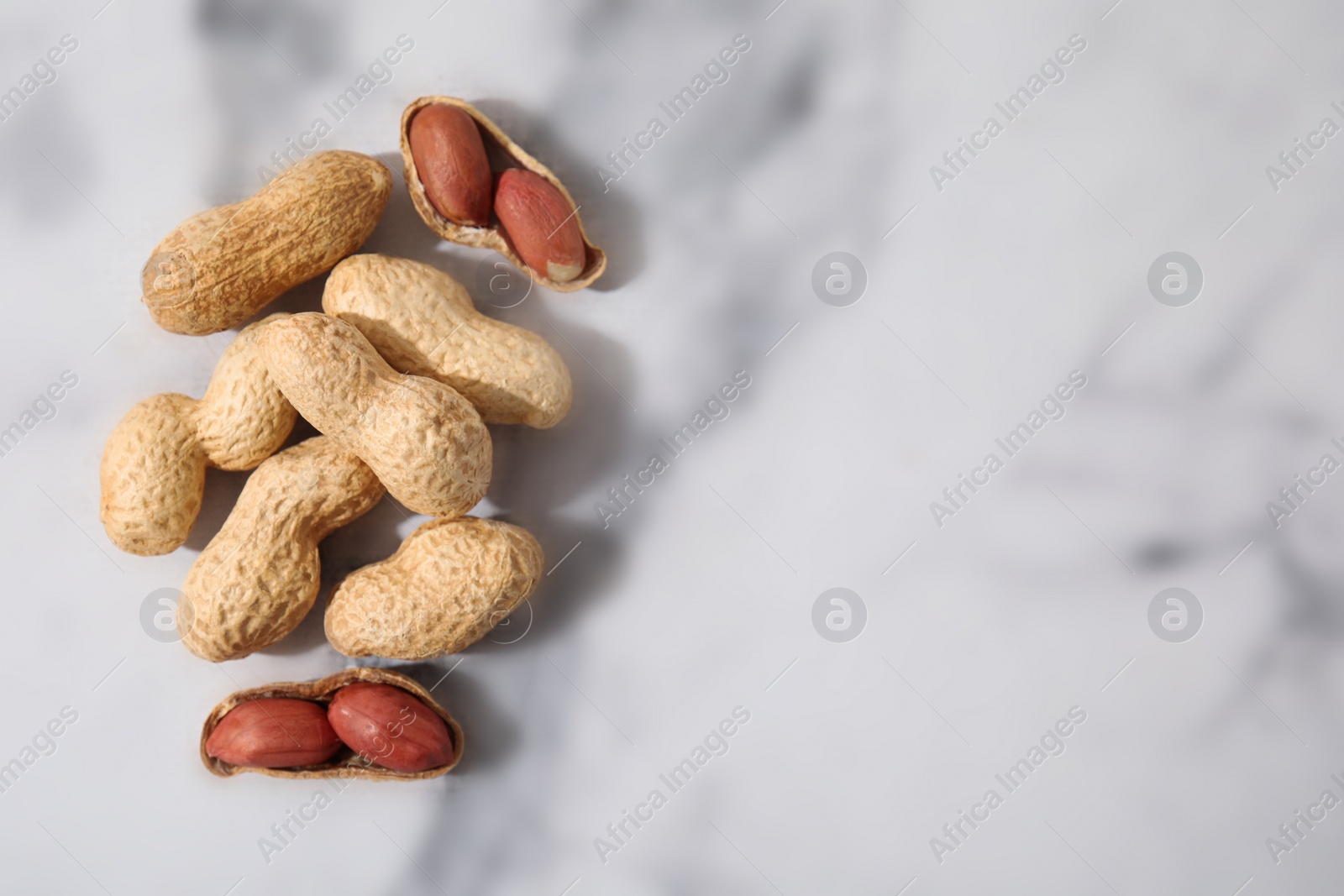 Photo of Fresh unpeeled peanuts on white marble table, top view. Space for text