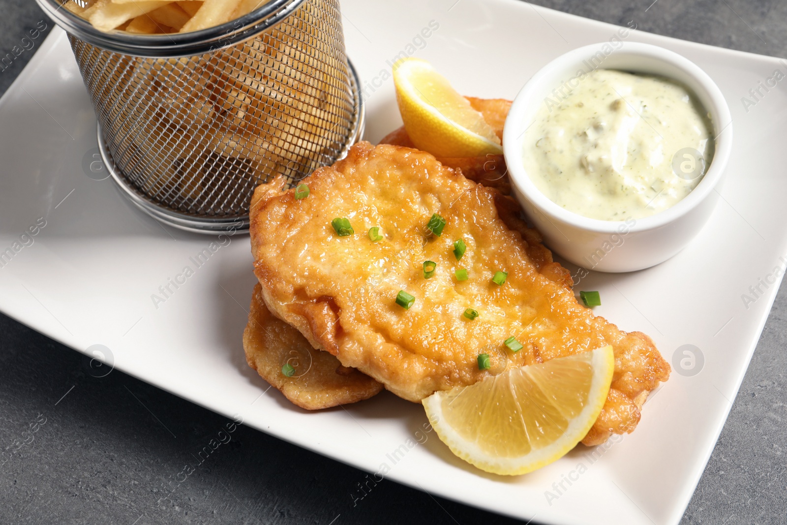 Photo of Plate with British traditional fish and potato chips on grey table