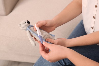 Young woman with toy bunny showing her mother pregnancy test, closeup. Grandparent reaction to future grandson