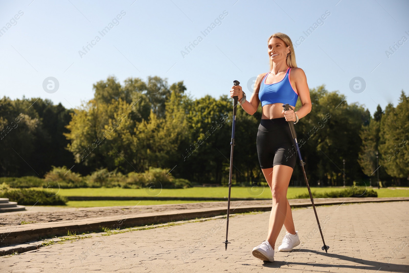 Photo of Happy woman practicing Nordic walking with poles in park on sunny day