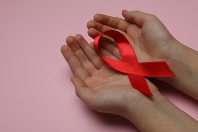 Photo of Little girl holding red ribbon on pink background, closeup. AIDS disease awareness