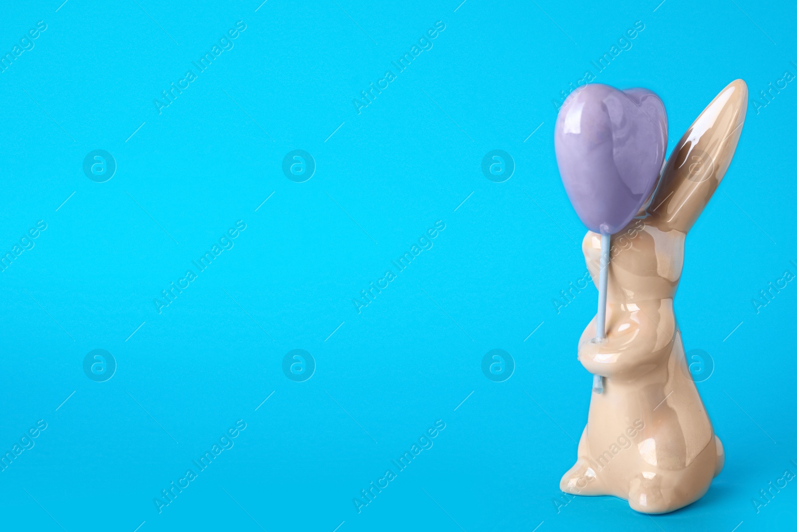 Photo of Bunny ceramic figure as Easter decor on blue background. Space for text