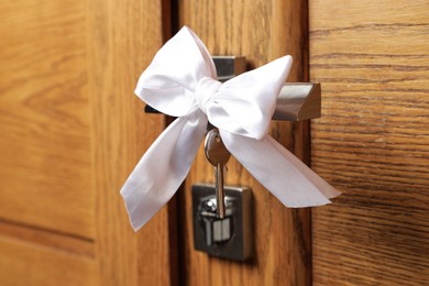 Key with white bow on door handle, closeup view. Housewarming party