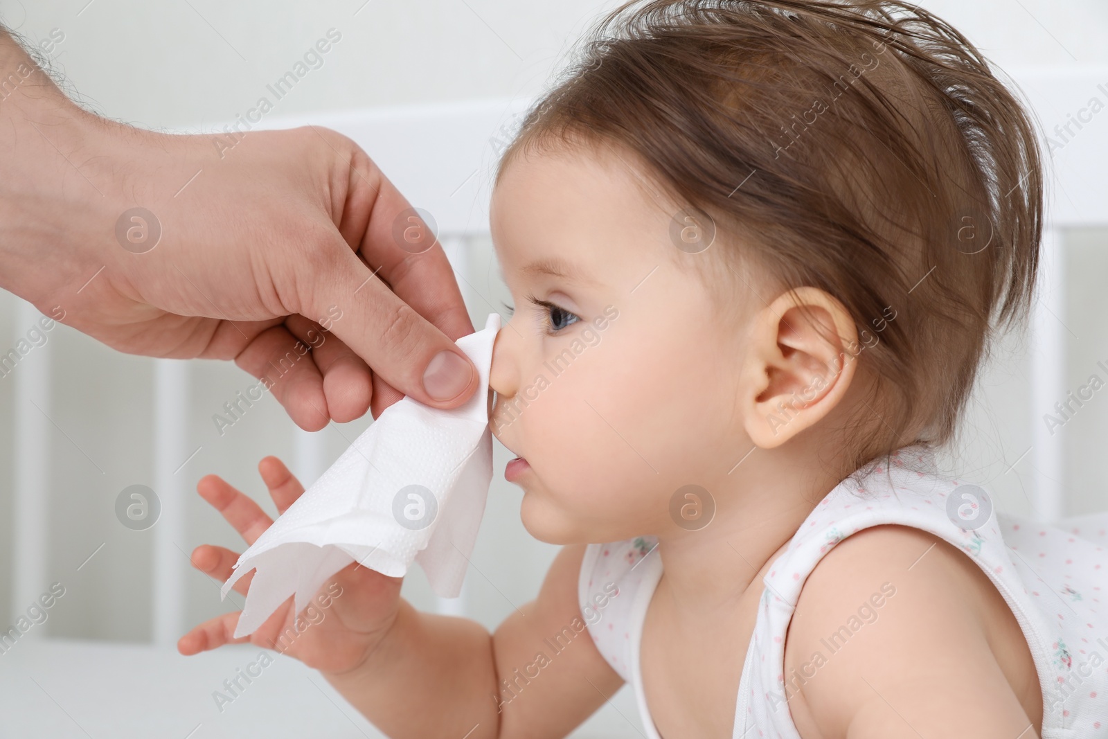 Photo of Father wiping runny nose of little baby with napkin on bed, closeup