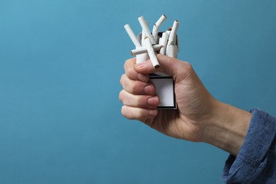 Photo of Stop smoking. Man holding pack with broken cigarettes on light blue background, closeup. Space for text