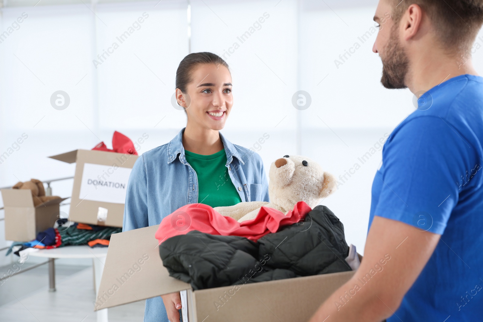 Photo of Young woman giving box with donations to male volunteer indoors