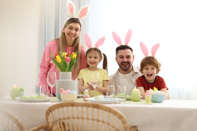 Easter celebration. Portrait of happy family with bunny ears at served table in room