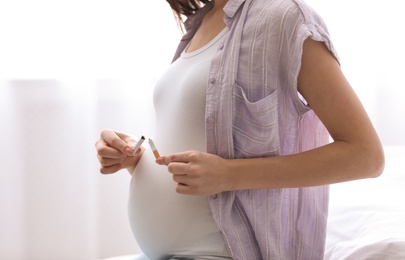 Photo of Young pregnant woman breaking cigarette at home, closeup