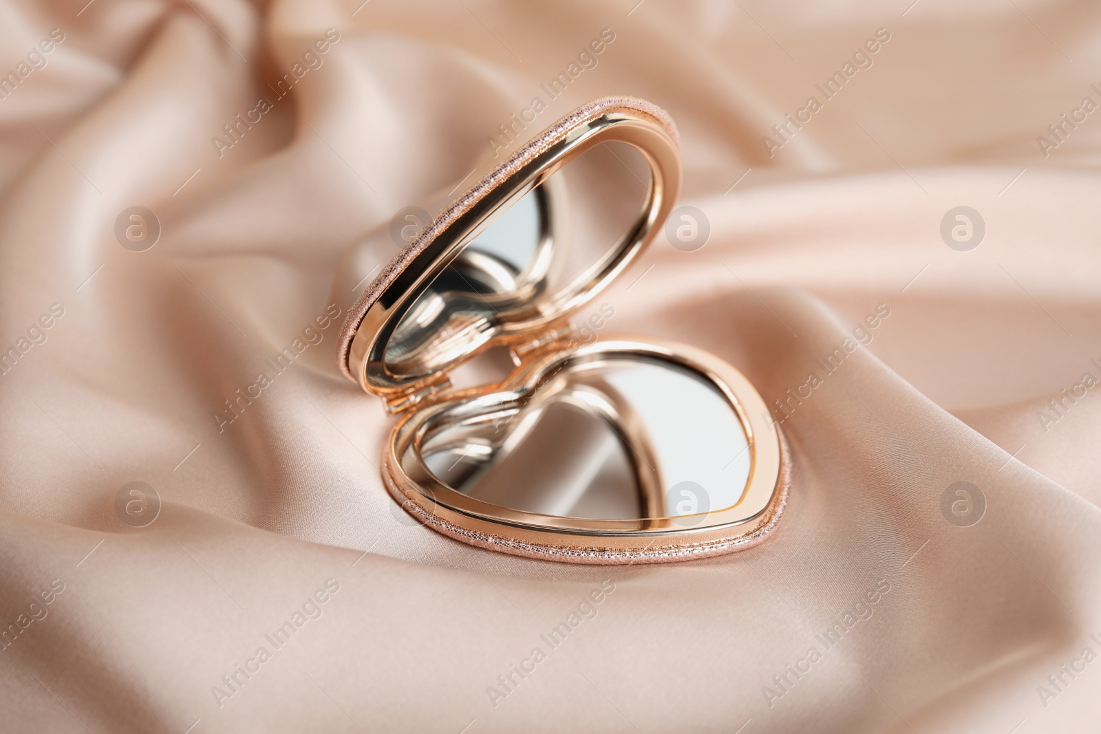 Photo of Stylish heart shaped cosmetic pocket mirror on rose gold fabric