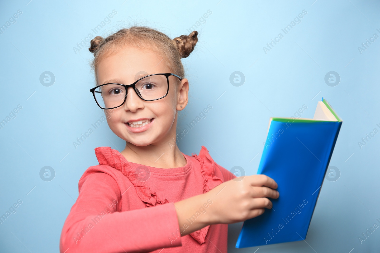 Photo of Cute little girl with glasses and textbook on light blue background