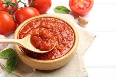 Photo of Homemade tomato sauce and spoon in bowl on white table, closeup