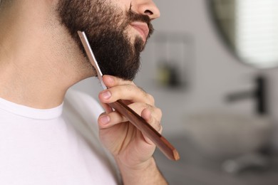 Handsome young man shaving beard with blade indoors, closeup