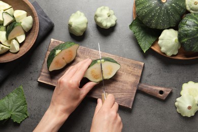 Woman cutting ripe green pattypan squash at grey table, top view