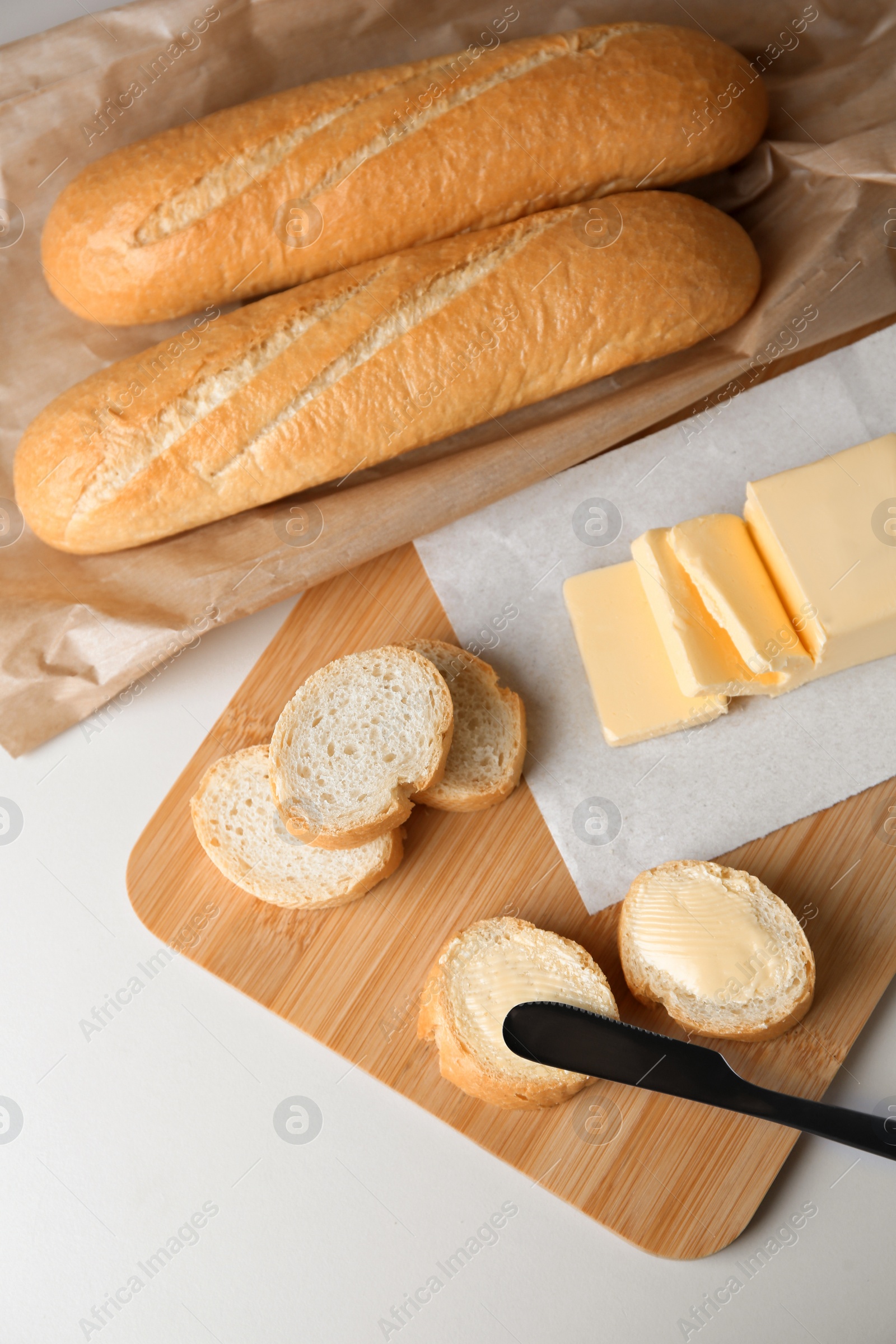 Photo of Tasty cut baguette with fresh butter on white table