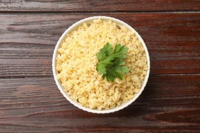 Delicious bulgur with parsley in bowl on wooden table, top view