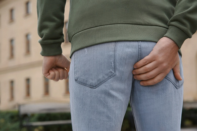 Man suffering from hemorrhoid pain outdoors, back view