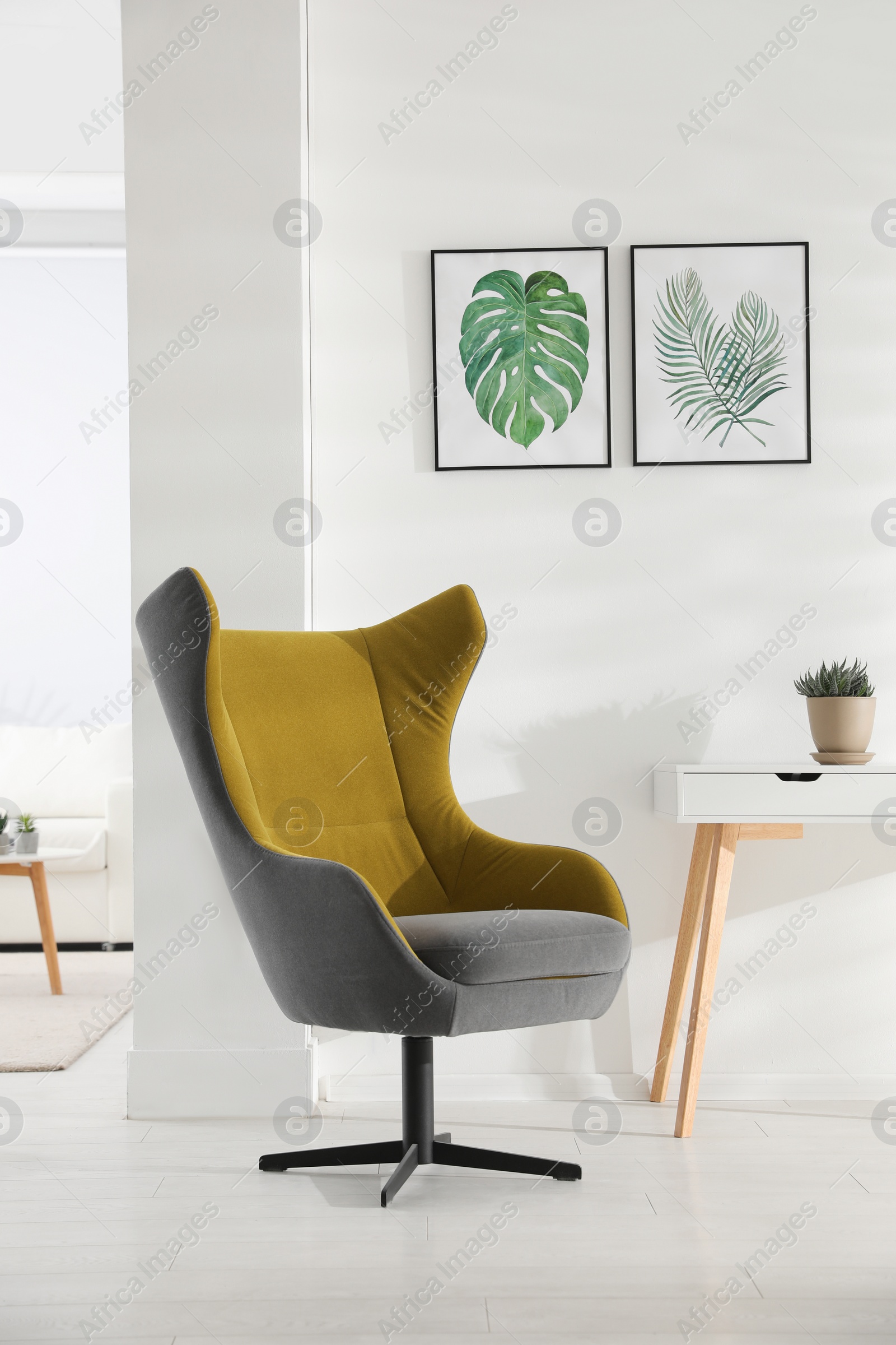 Photo of Stylish room interior with comfortable armchair and paintings of tropical leaves