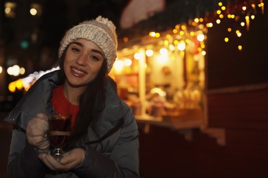 Woman with glass cup of mulled wine at winter fair. Space for text