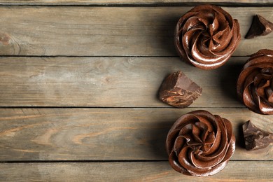 Photo of Delicious chocolate cupcakes with cream on wooden table, flat lay. Space for text