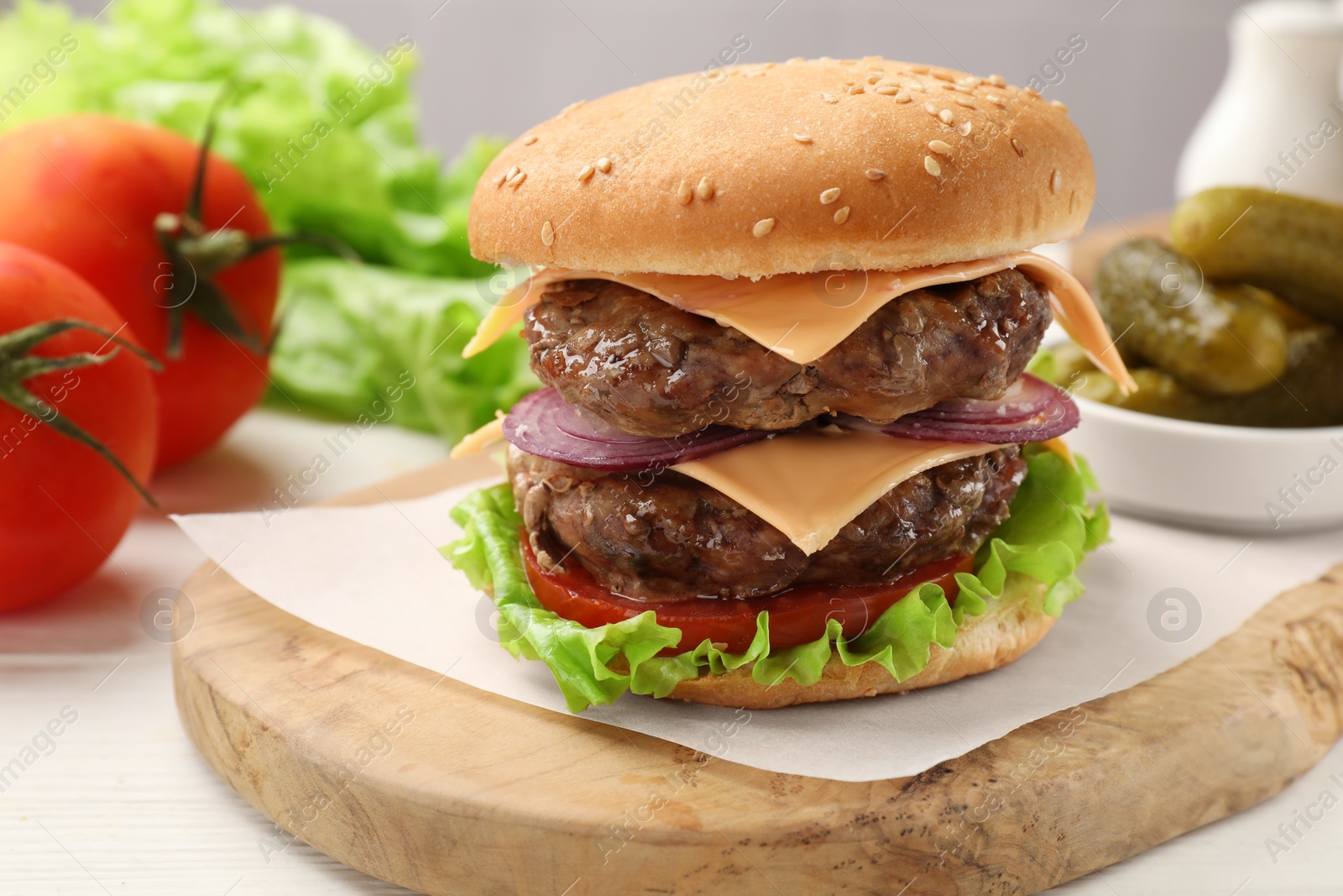 Photo of Tasty hamburger with patties, cheese and vegetables on table