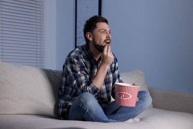 Photo of Emotional man eating popcorn while watching TV at home in evening