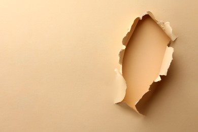 Photo of Hole in light beige paper on color background, space for text