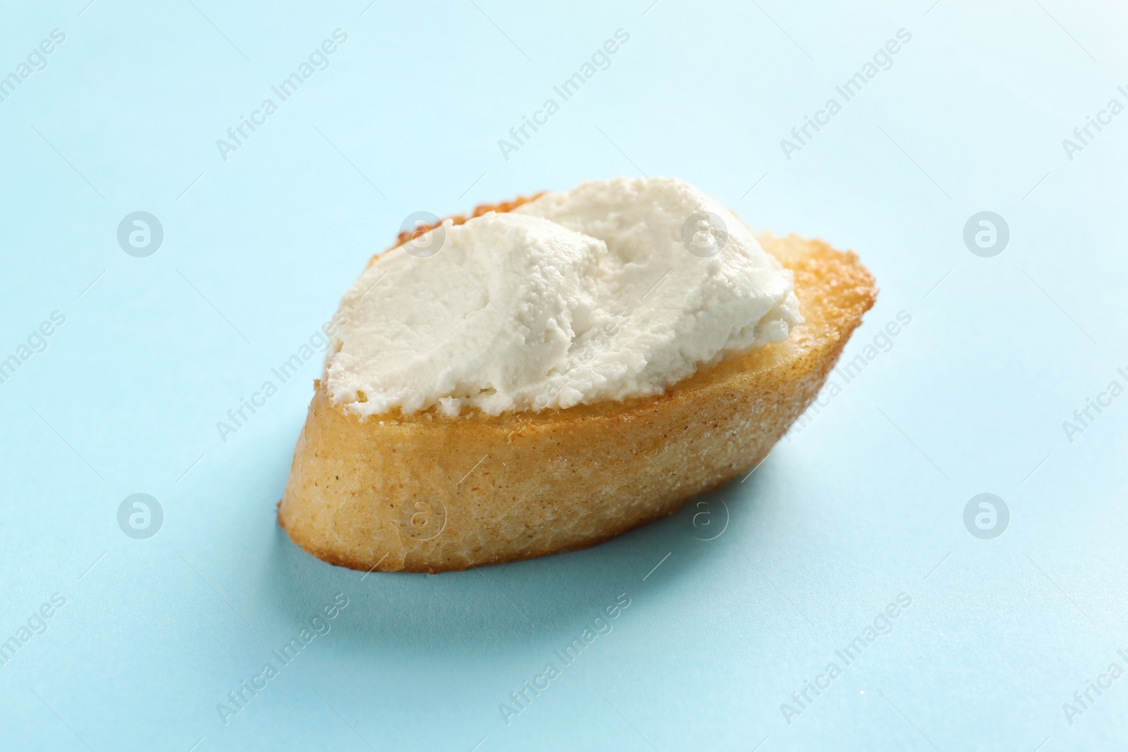 Photo of Piece of baguette with tasty cream cheese on color background