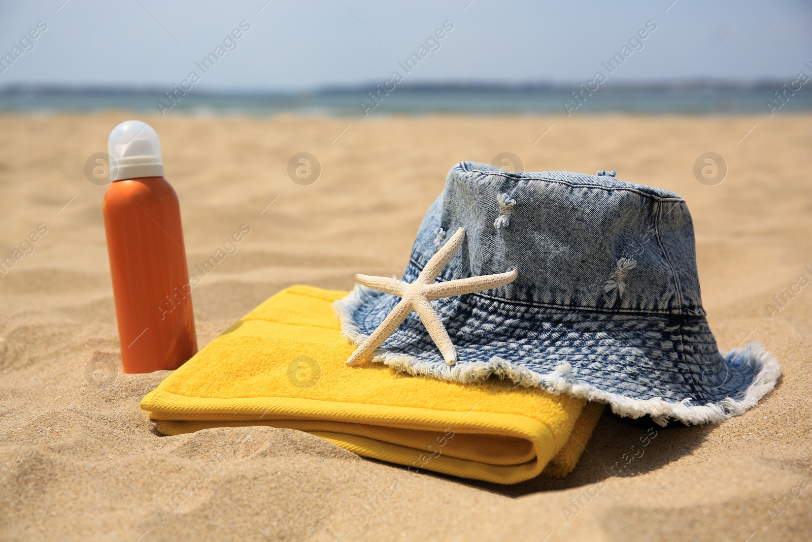 Photo of Sunscreen, panama hat, starfish and towel on sandy beach. Sun protection