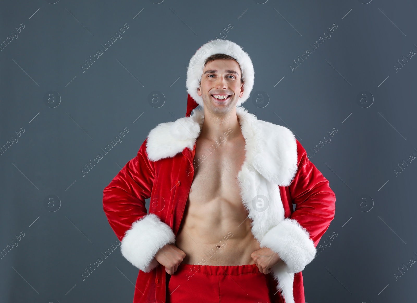 Photo of Young muscular man in Santa Claus costume  on gray background