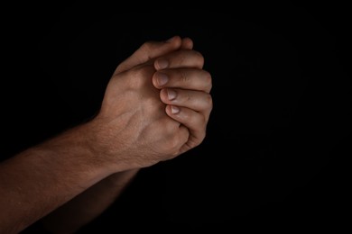 Man praying against black background, closeup view