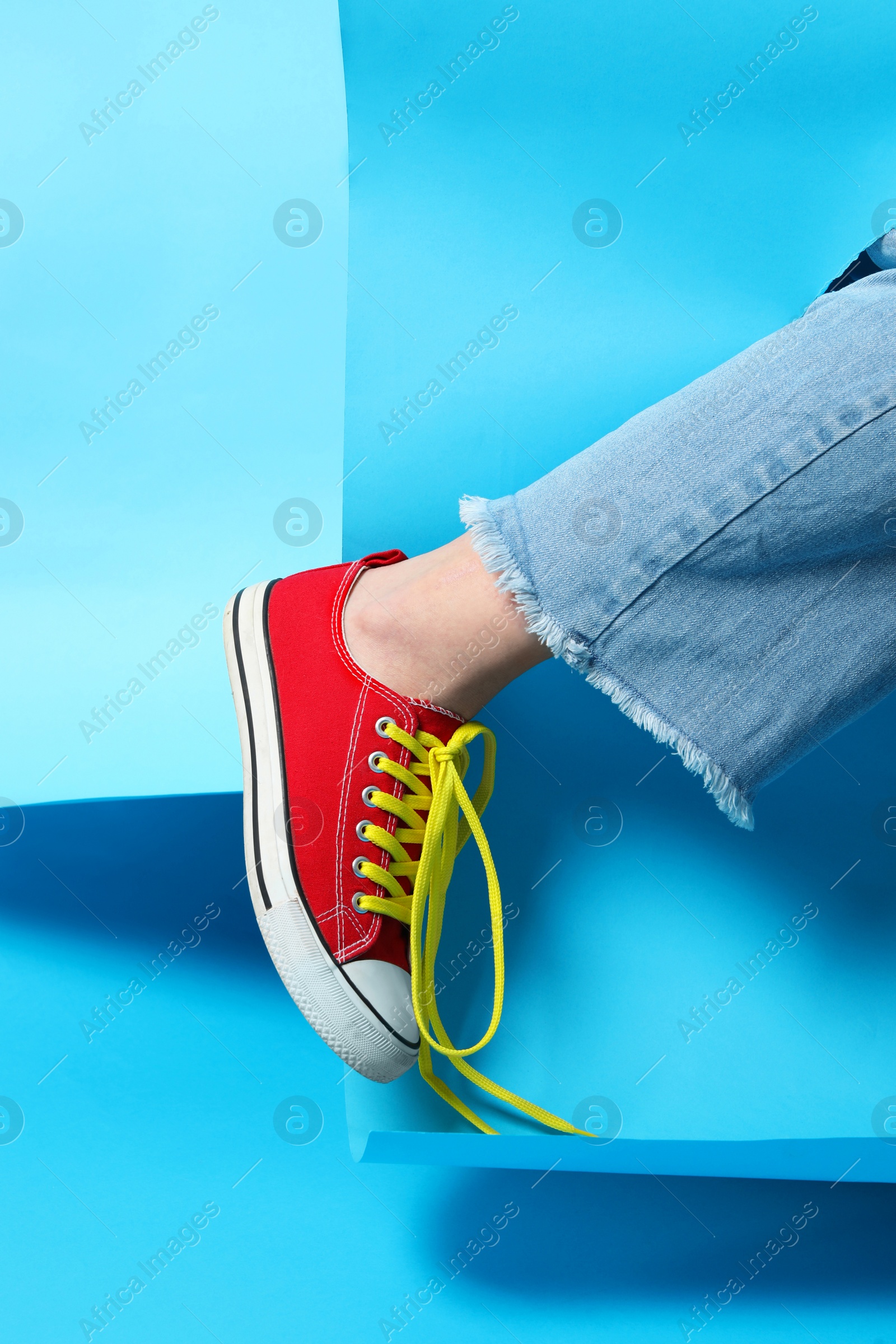 Photo of Woman wearing stylish shoes with yellow laces on light blue background, closeup