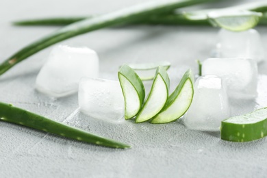 Slices of aloe vera and ice cubes on gray table