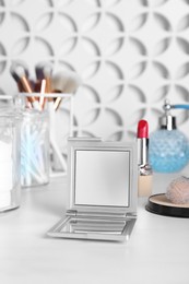 Stylish pocket mirror and cosmetic products on white table